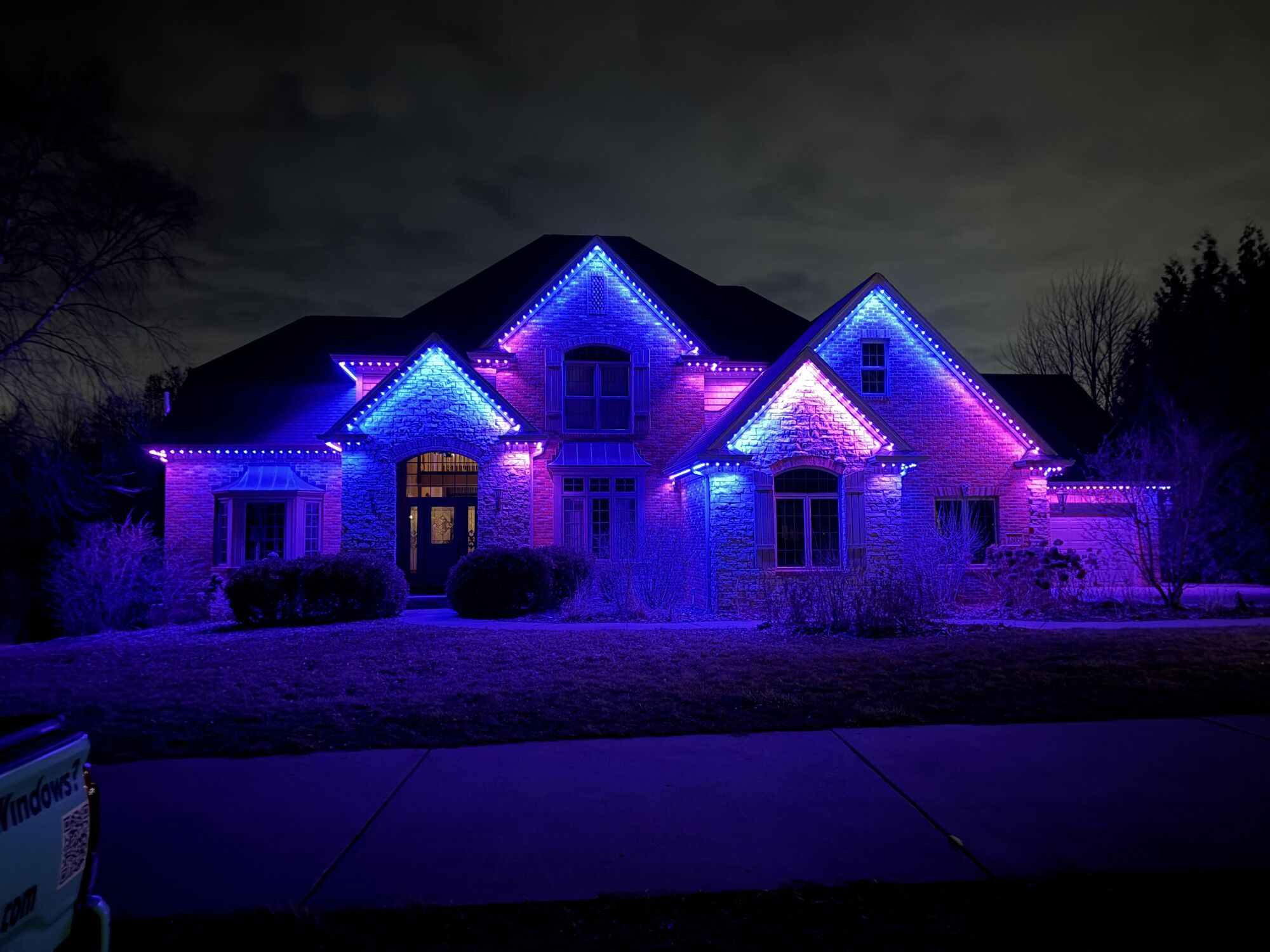 The same brick home lit in deep violet, blue and pink along the rooflines