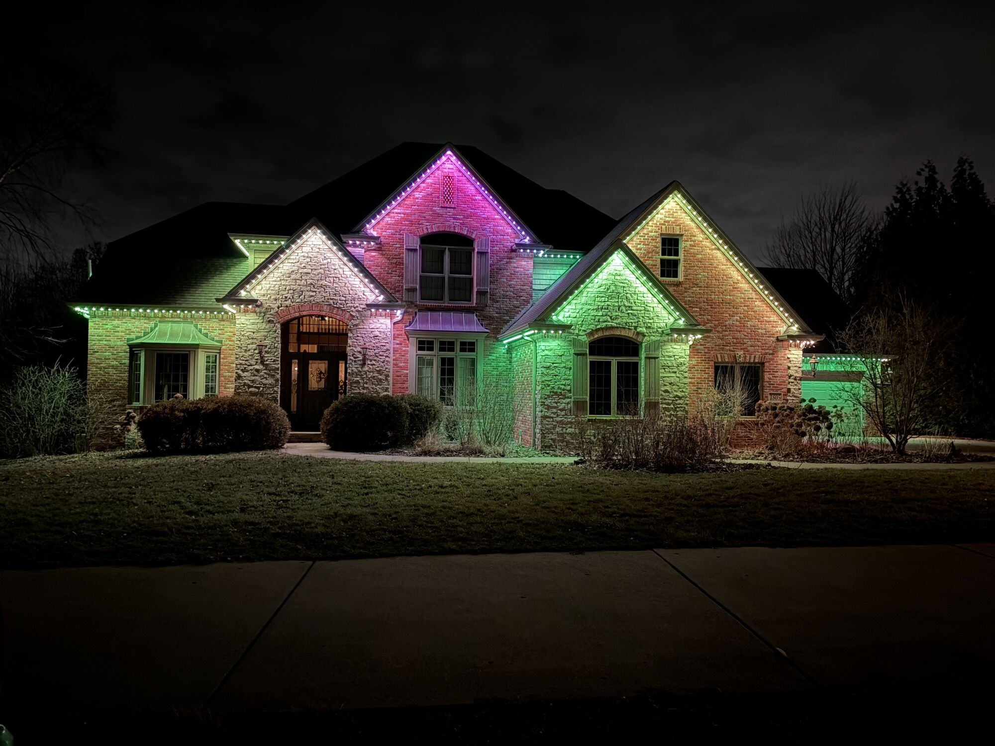 Brick home with green and pink lighting outlining its layered rooflines