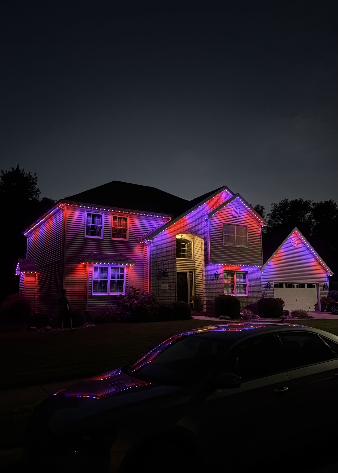Two-story home at dusk with pink, red and violet lighting along its gables