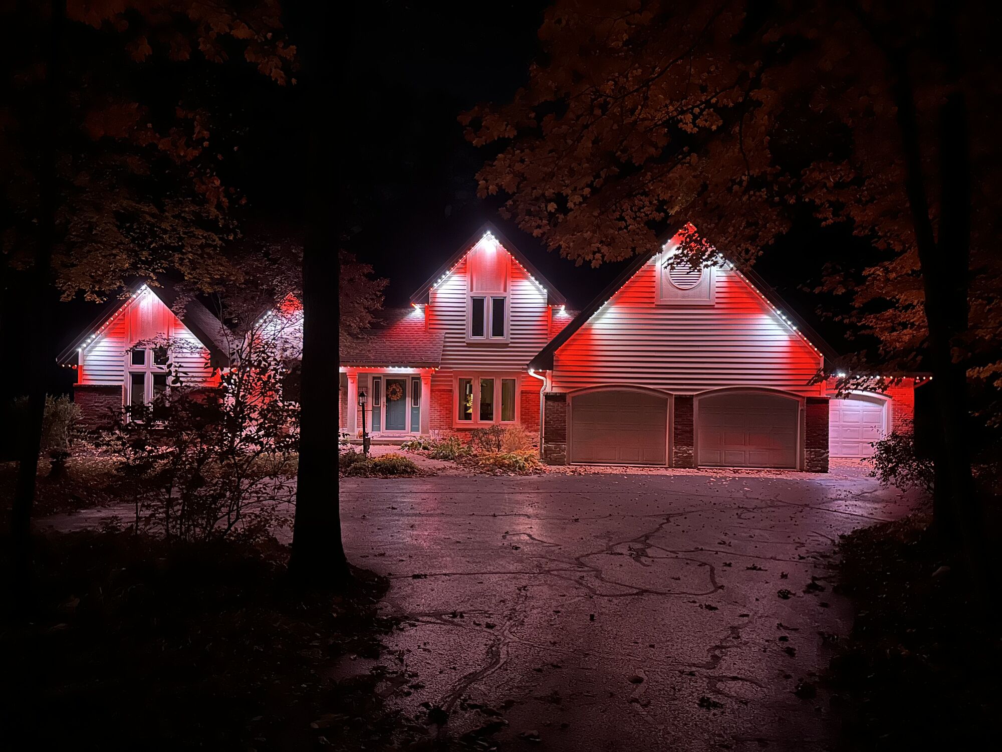 Home framed by trees with deep red lighting along its gables reflecting on a wet driveway