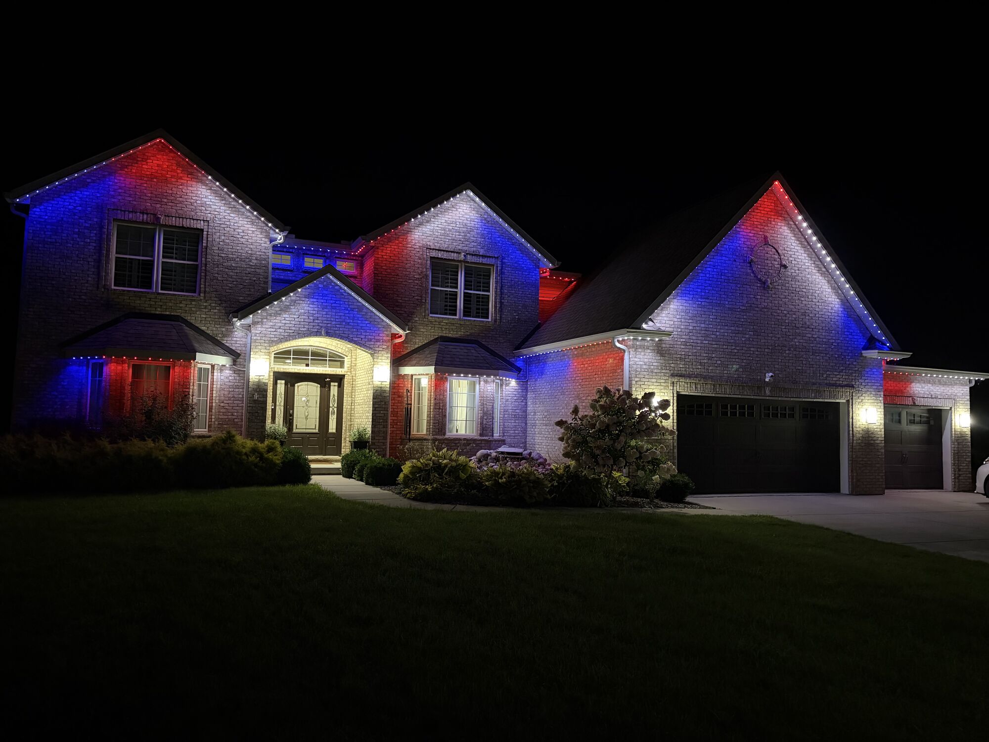 Large brick two-story home at night with red, white and blue lighting along every roofline and gable