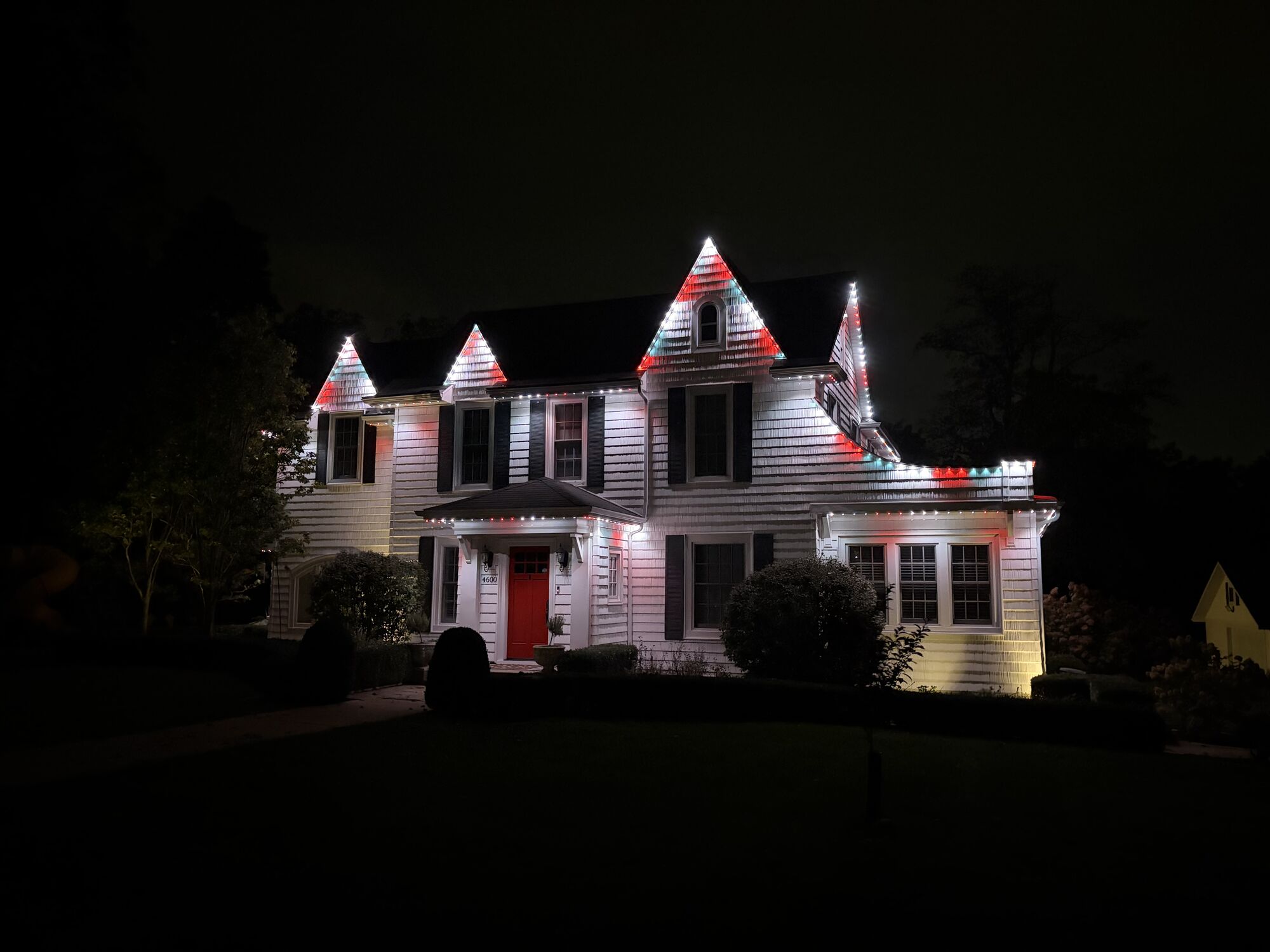 White Victorian-style home with red and white lights accenting its pointed gables