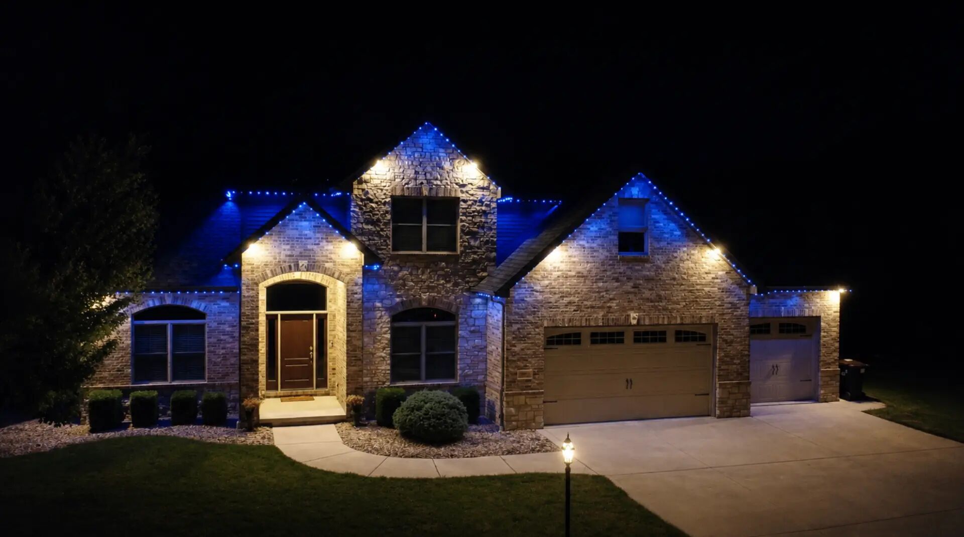 Stone home with blue roofline lighting and warm white accents over the entry and garage