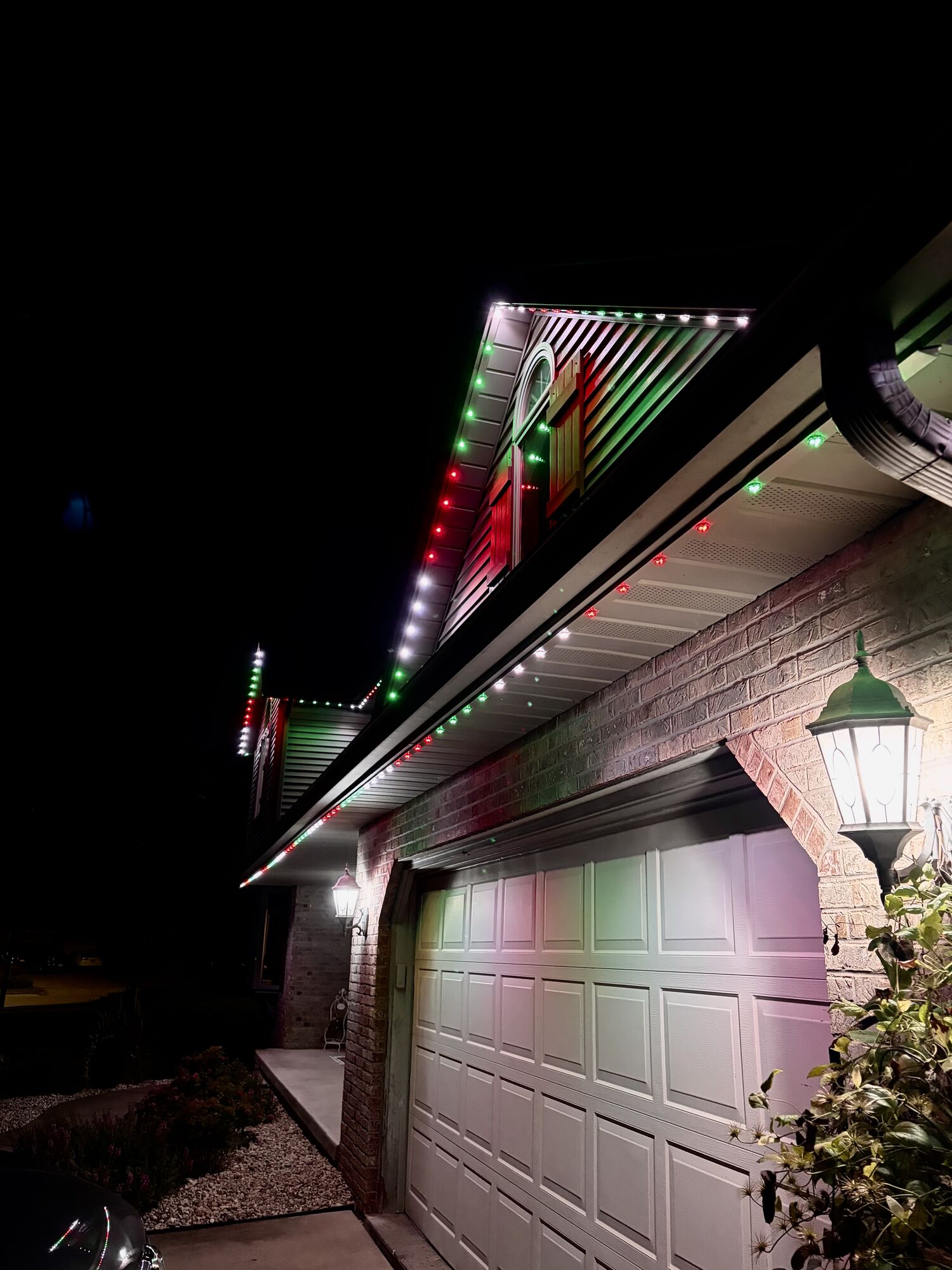 Close view of evenly spaced lights beneath the eaves above a garage, shifting from white to red and green